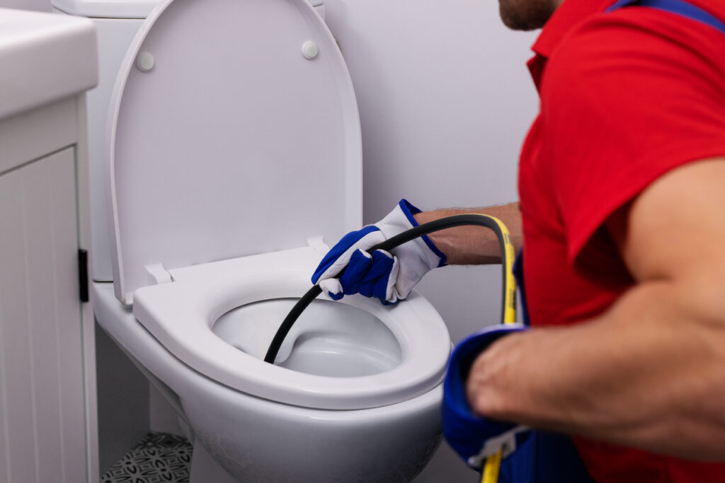 plumber unclogging blocked toilet with hydro jetting at home bathroom during sewer cleaning service
