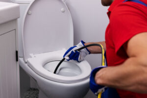 Plumber unclogging blocked toilet with hydro jetting at home bathroom.