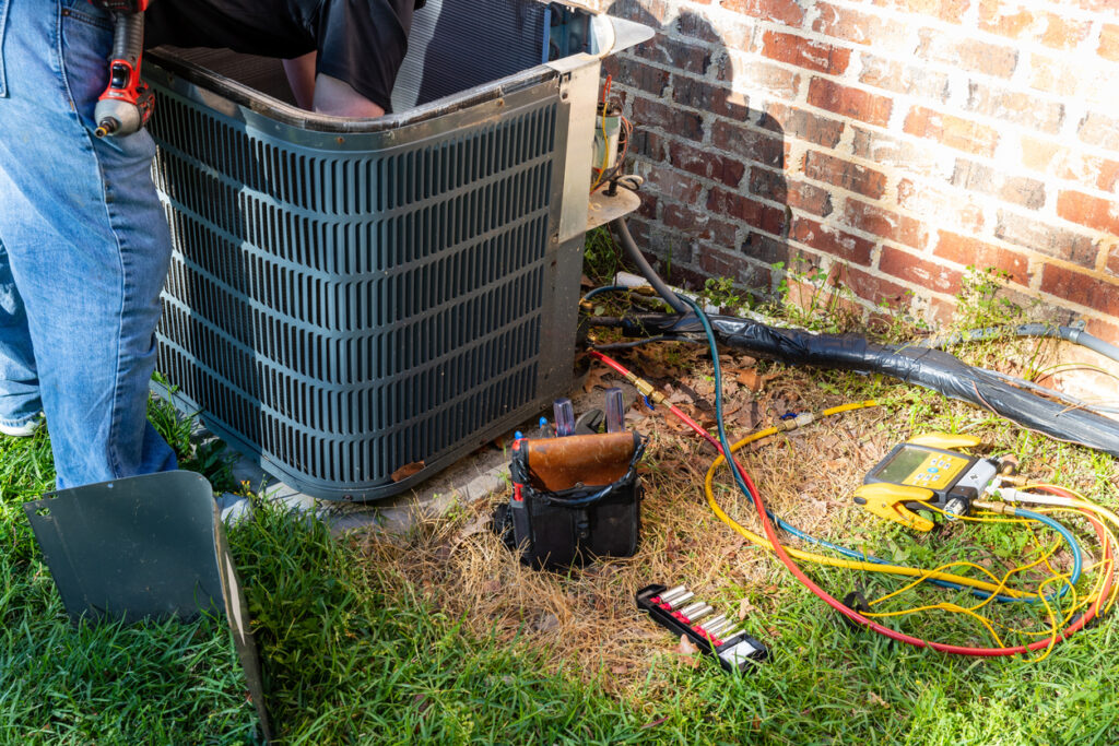 Air conditioner maintenance being performed on HVAC unit outside brick home.