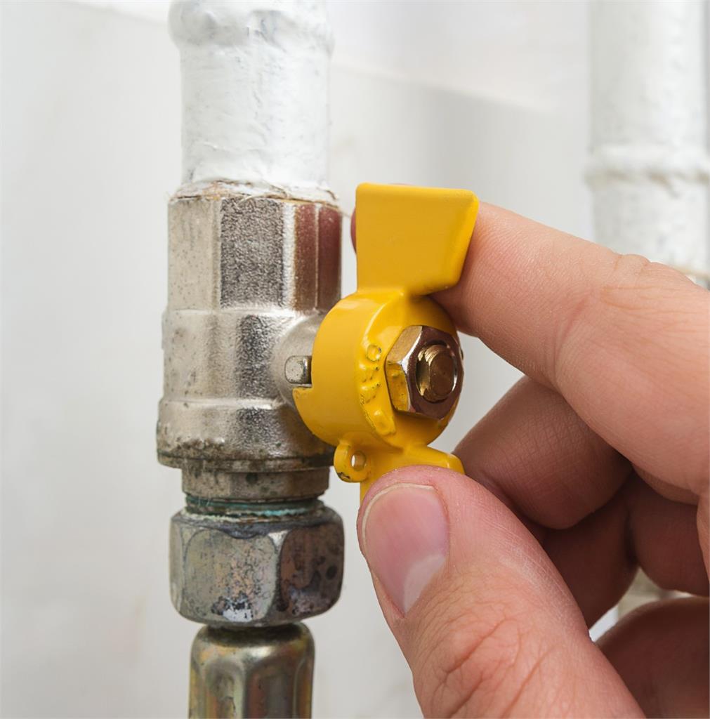 Up close of person's hand as they shut off the yellow gas valve in their home